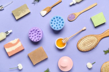 Saç derisi masaj aletleri, şampuan çubukları, bir kase bal ve mor arka planda deniz tuzu.