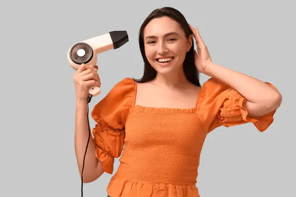 Beautiful young woman with hair dryer on light background