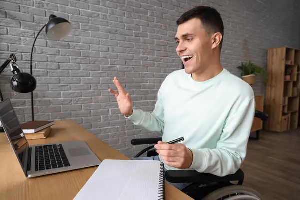 Happy young man in wheelchair with laptop at home