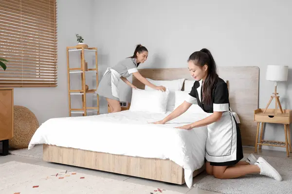 Young chambermaids making bed in bedroom