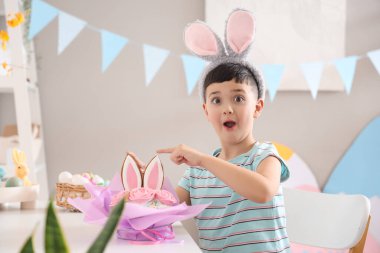 Şok olmuş tavşan kulaklı küçük çocuk evdeki paskalya pastasını işaret ediyor.