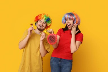 Komik kılık değiştirmiş genç arkadaşlar osuruk yastığı ve sarı arka planda ıslık çalıyorlar. 1 Nisan kutlamaları