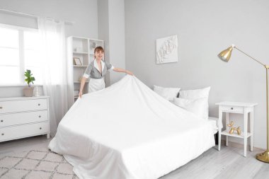 Genç oda hizmetçisi yatak odasını topluyor.