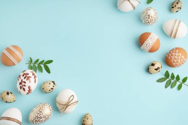 Süslü Paskalya yumurtaları ve mavi arka planda yapraklardan yapılmış çerçeve