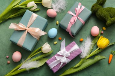 Hediye kutularıyla Paskalya yumurtaları, lale çiçekleri ve grunge yeşili arka planda tavşan.