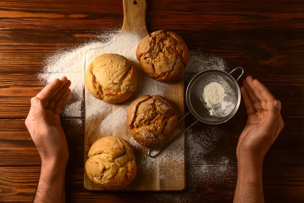 Taze lezzetli çörekleri olan ve ahşap arka planda un taşıyan erkek eller.