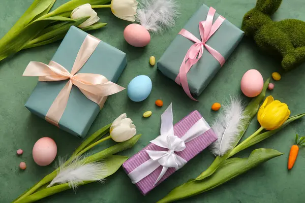 Hediye kutularıyla Paskalya yumurtaları, lale çiçekleri ve grunge yeşili arka planda tavşan.