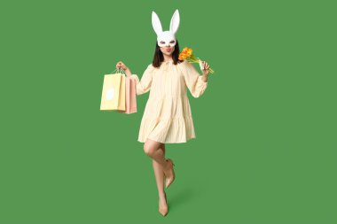 Alışveriş torbaları ve yeşil arka planda öpüşen bir buket çiçekle tavşan kulaklı güzel bir genç kadın. Paskalya kutlaması
