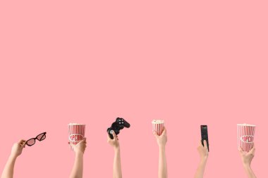 Patlamış mısır, televizyon kumandası, oyun bloknotu ve pembe arka planda 3D gözlük tutan eller.