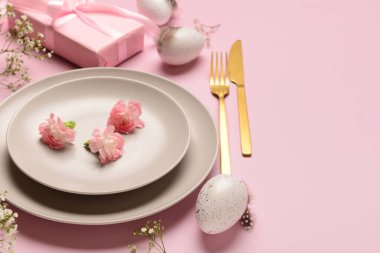 Şirin Paskalya sofrası, pembe arka planda hediyeler, çiçekler ve yumurtalar.