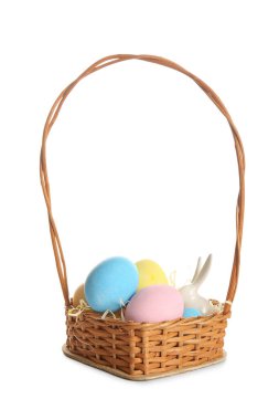 Beyaz arka planda boyanmış Paskalya yumurtaları ve seramik tavşanlı hasır sepet.