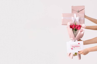 Pembe lale buketi, hediye kutusu ve beyaz arka planda bayram kartpostalı olan kadın elleri. Uluslararası Kadınlar Günü için Alışveriş