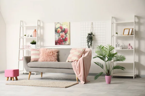 Loft style interior of living room with stylish sofa, houseplant, shelves and picture