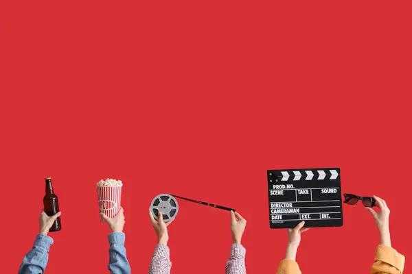 Many hands with bucket of popcorn, movie clapper and film reel on red background