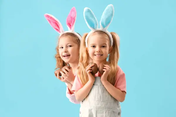 在兔子耳朵里可爱的小女孩 有蓝色背景的巧克力复活节彩蛋 — 图库照片