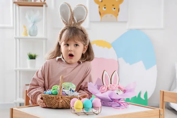 Evde paskalya yumurtası ve kekle tavşan kulağı takan küçük bir kız.