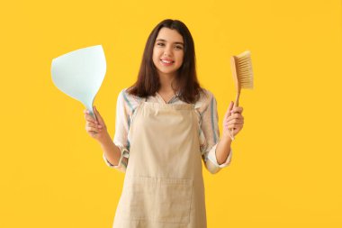 Sarı arka planda faraş ve fırçayla genç bir kadın.