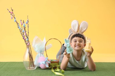 Cute little boy wearing bunny ears with Easter rabbits, basket and pussy willow branches on yellow background