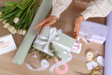 Hediye kutularıyla kadın elleri, paketleme malzemeleri ve ahşap masada güzel çiçekler. Uluslararası Kadınlar Günü