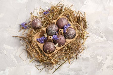Çiçekli Paskalya yumurtaları ve gri arka planda saman.