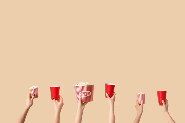 Hands holding buckets with popcorn and cups on beige background