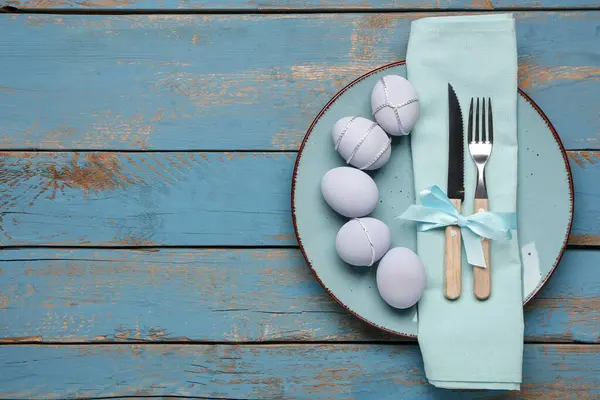 Mavi ahşap arka planda boyanmış Paskalya yumurtaları, peçete ve çatal bıçak seti ile güzel bir masa.