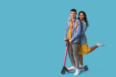 Mavi arka planda modern elektrikli scooter kullanan güzel genç bir çift.