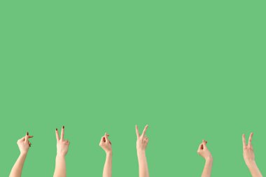 Kadın elleri barış jestleri gösteriyor ve yeşil arka planda bir şey tutuyor.