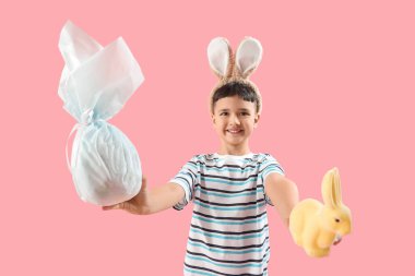 Paskalya hediyesi yumurtası ve pembe arka planda bir tavşanla tavşan kulağı takan sevimli bir çocuk.