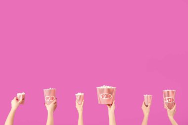 Pembe arka planda patlamış mısırlı kovaları tutan eller