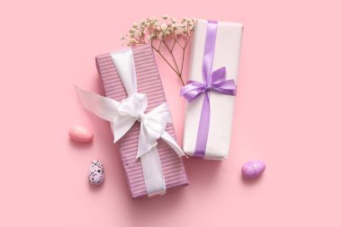 Paskalya yumurtaları, çingene çiçekleri ve pembe arka planda hediye kutuları.
