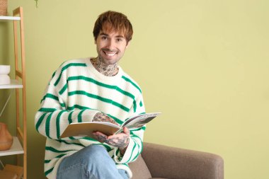 Yakışıklı adam evdeki yumuşak koltukta dergi okuyor.