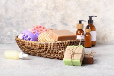 Saç derisi masaj sepetleri, şampuan barları ve grunge grisi arka planda banyo malzemeleri.