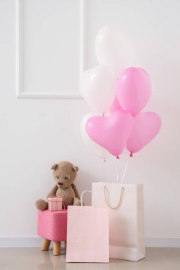 Oyuncak ayılı puf, alışveriş torbaları ve beyaz duvarın yanında kalp şeklinde balonlar. Sevgililer Günü kutlaması