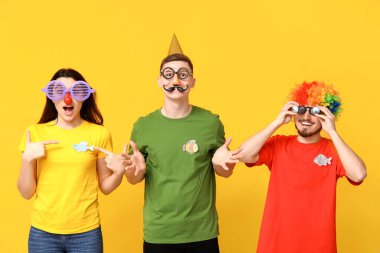 Sarı arka planda kağıt balıklarıyla komik kılık değiştirmiş genç arkadaşlar. 1 Nisan kutlamaları