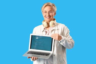 Mavi arka planda dizüstü bilgisayarı olan olgun bir kadın programcı.