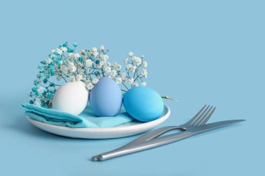 Mavi arka planda yumurta ve çiçeklerle Paskalya için güzel bir sofra.