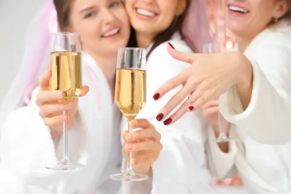 Young woman with engagement ring and her bridesmaids drinking champagne at Hen Party in bedroom, closeup