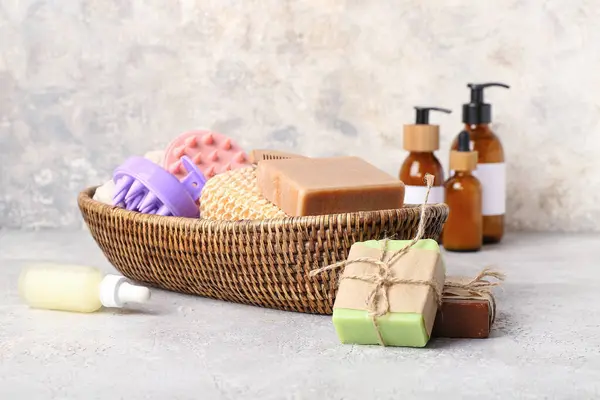 Saç derisi masaj sepetleri, şampuan barları ve grunge grisi arka planda banyo malzemeleri.