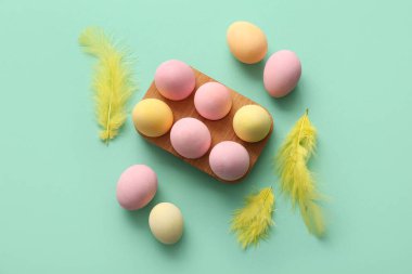 Boyanmış Paskalya yumurtaları ve turkuaz arka planda tüyleri olan ahşap tutucu.