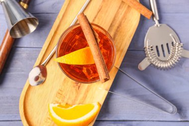 Lezzetli bir bardak eski moda kokteyl ve mavi ahşap arka planda portakal dilimleri.