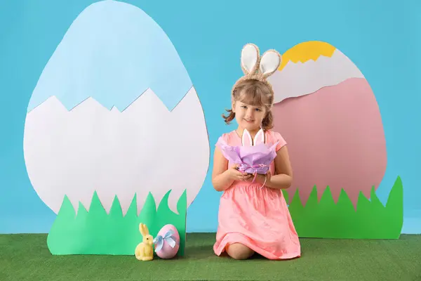 可爱的小女孩 戴着兔子耳朵 戴着复活节蛋糕和蓝色背景的装饰品 — 图库照片