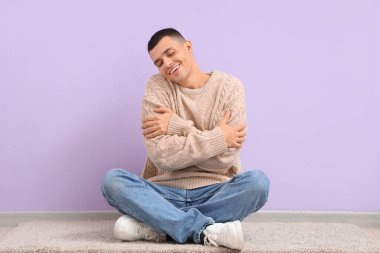 Genç adam leylak duvarın yanında kendine sarılıyor.