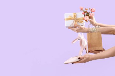 Hediye kutusu olan kadın elleri, yüksek topuklu ayakkabılar ve leylak arka planda çiçekler. Uluslararası Kadınlar Günü için Alışveriş