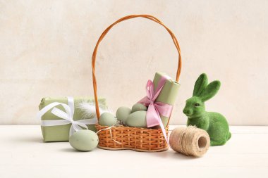 Boyanmış Paskalya yumurtaları, hediye kutuları ve beyaz ahşap masada oyuncak tavşancıklarla dolu bir sepet.