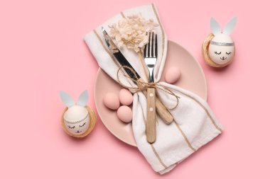 Paskalya yumurtaları, peçeteler ve pembe arka planda çatal bıçaklarla güzel bir masa.