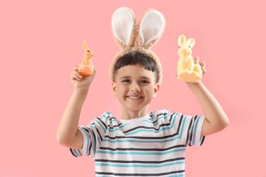 Pembe arka planda Paskalya tavşanlarıyla tavşan kulağı takan şirin bir çocuk.