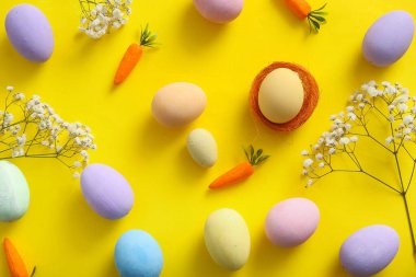 Sarı arka planda çikila çiçekli ve havuçlu Paskalya yumurtaları.