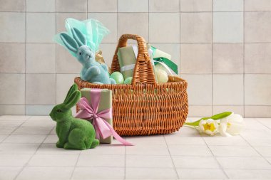 Boyanmış Paskalya yumurtaları, oyuncak tavşanlar ve beyaz fayanslı hediye kutuları olan hasır sepet.