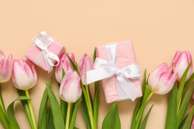 Bej arka planda hediye kutuları olan pembe laleler.